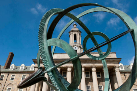 Green metal sculpture in front of Old Main building with blue sky.