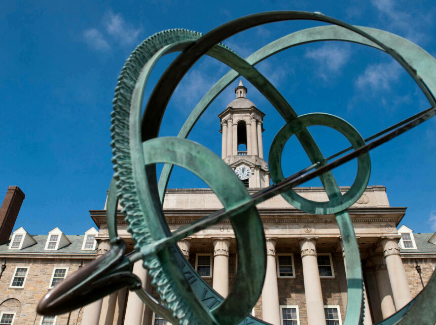 Green metal sculpture in front of Old Main building with blue sky.